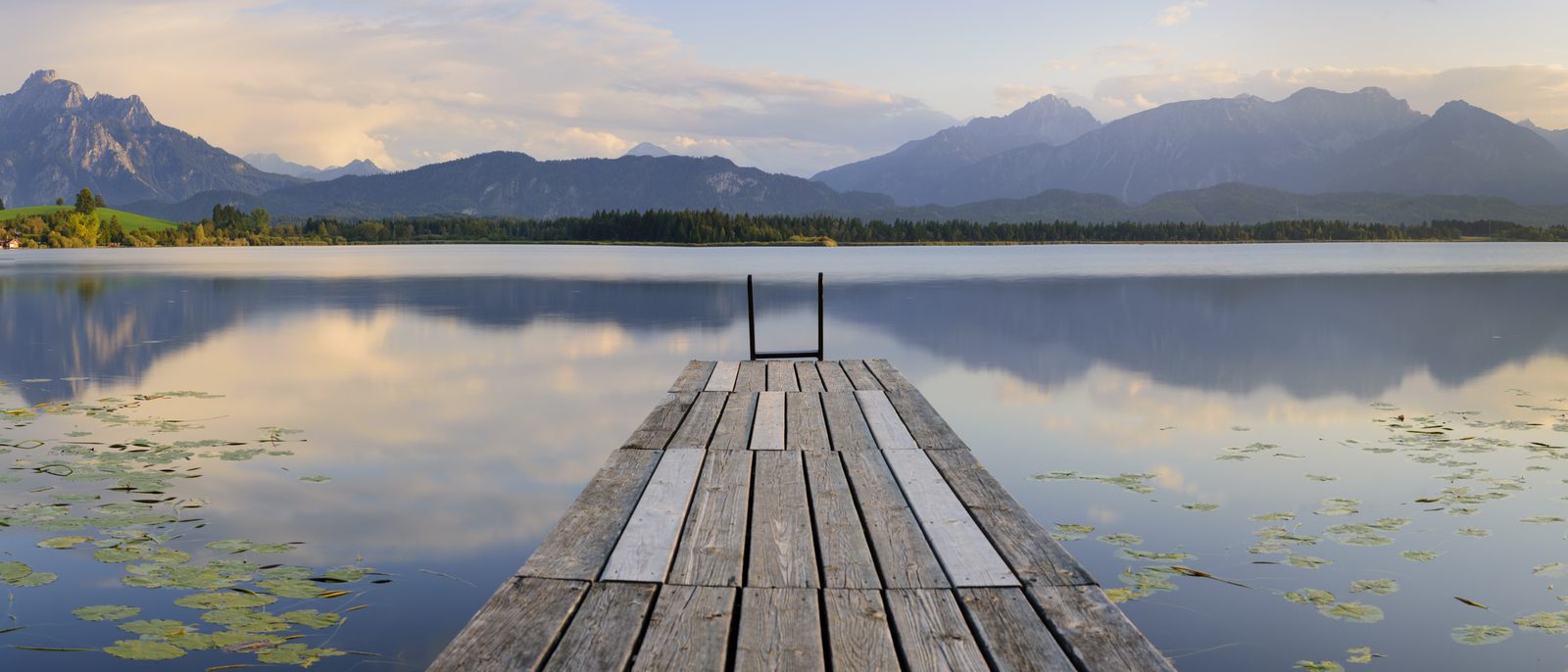 Steg an einem ruhigen See, im Hintergrund Berge